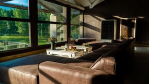 A spacious living room with large windows, a leather sofa, a coffee table, and a view of a green landscape. - Casa Septem (Tunuyan)