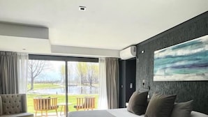 A modern hotel room with a large bed, a sofa, and a view of a garden and pool. - Casa Septem (Tunuyan)