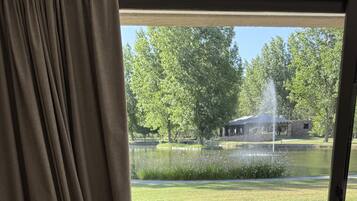Ein Zimmer mit einem gepolsterten Sessel, einem gelben Hocker und Blick auf eine Terrasse mit Holzmöbeln und einem Teich.
