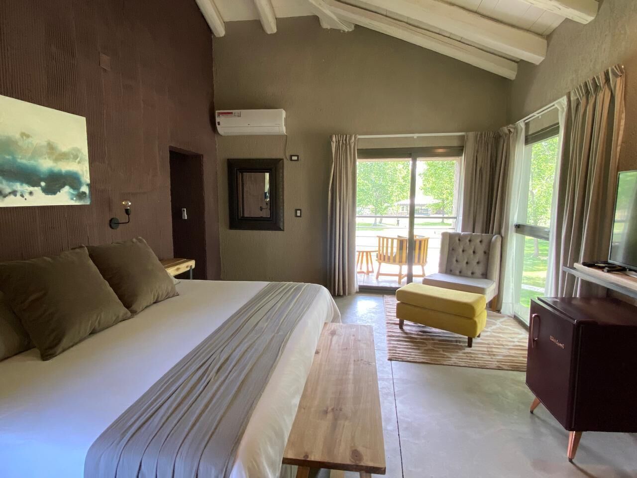 Un dormitorio con una cama grande, un banco de madera, un televisor y vistas al exterior.