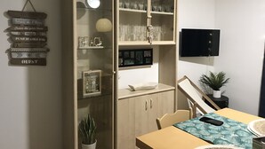 Un coin repas comprenant une table en bois, des chaises, un téléviseur fixé au mur et un bar avec des verres.