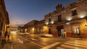 A street view at dusk with historic buildings, a crosswalk, and pedestrians. - OYO Hostal Mich Morelia (Morelia)