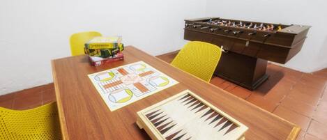 A wooden table with a foosball table, a board game, and a yellow chair.