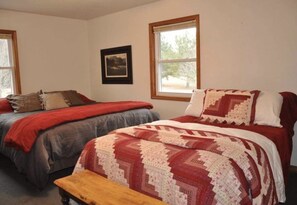 A room with two beds, each with a patterned blanket, a wooden bench, and a framed picture on the wall.