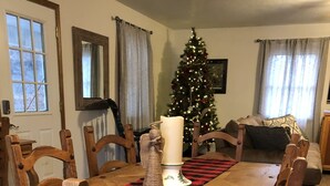 Een eetruimte met een houten tafel, stoelen, een kerstboom en een kaarsen decoratie in het midden.