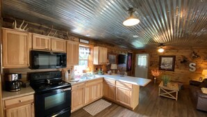 A rustic cabin interior with wooden cabinets, a black stove, a microwave, a sink, and a ceiling with exposed beams. - AMAZING VIEW of Mount Magazine! (Booneville)