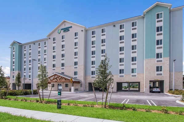 A multi-story hotel with a modern design, featuring a central entrance with a covered area and parking spaces in front.