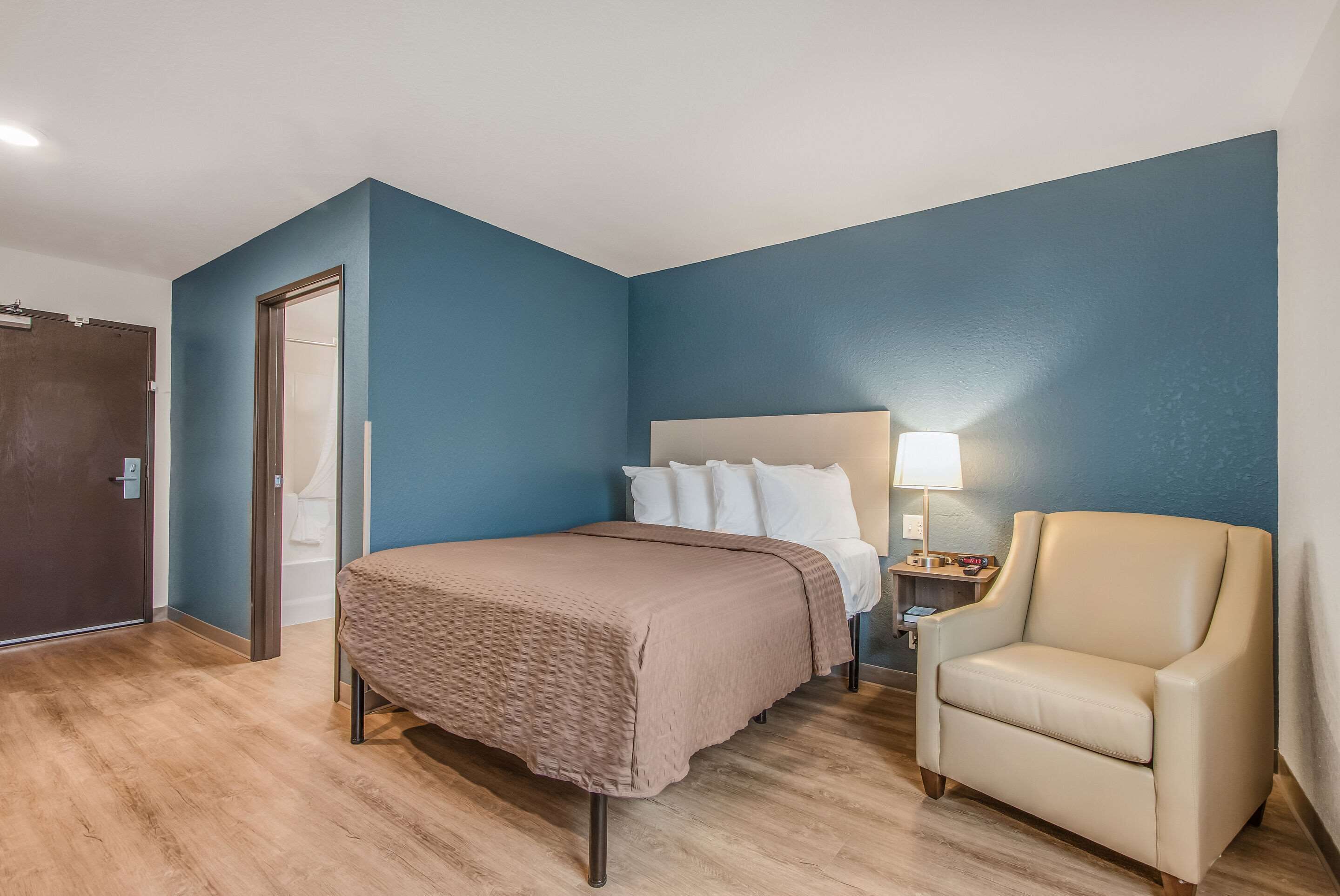 Una habitación de hotel con una cama, una silla, una mesita de noche y una lámpara.