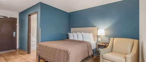A hotel room with a bed, a chair, a nightstand, and a lamp.