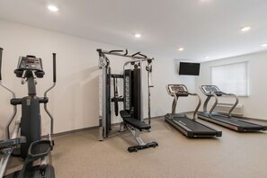 A gym with cardio machines, weight training equipment, and a TV on the wall.