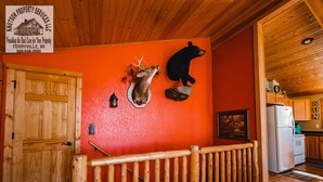Ein Blockhaus-Interieur mit Holzboden, einem aufgehängten Hirschkopf, einem Bärenkopf und einer Küchenzeile.