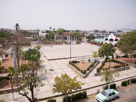 Una amplia plaza con un espacio central abierto, rodeada de árboles y bancos.