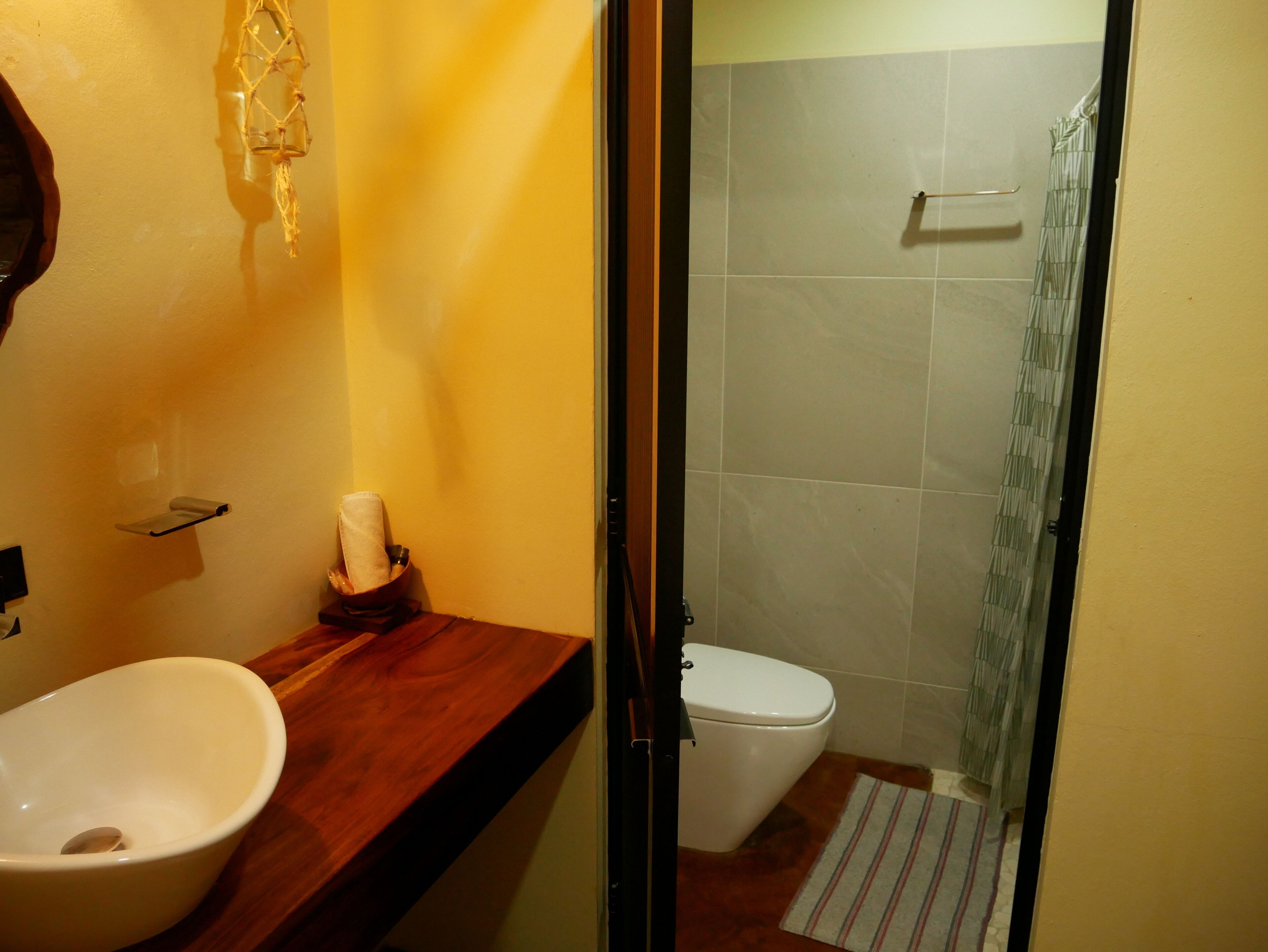 A bathroom with a wooden vanity, a white sink, a toilet, and a shower with a striped curtain.
