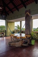 Un amplio espacio al aire libre con una mesa de madera rodeada de sillas, una hamaca y una planta en maceta.