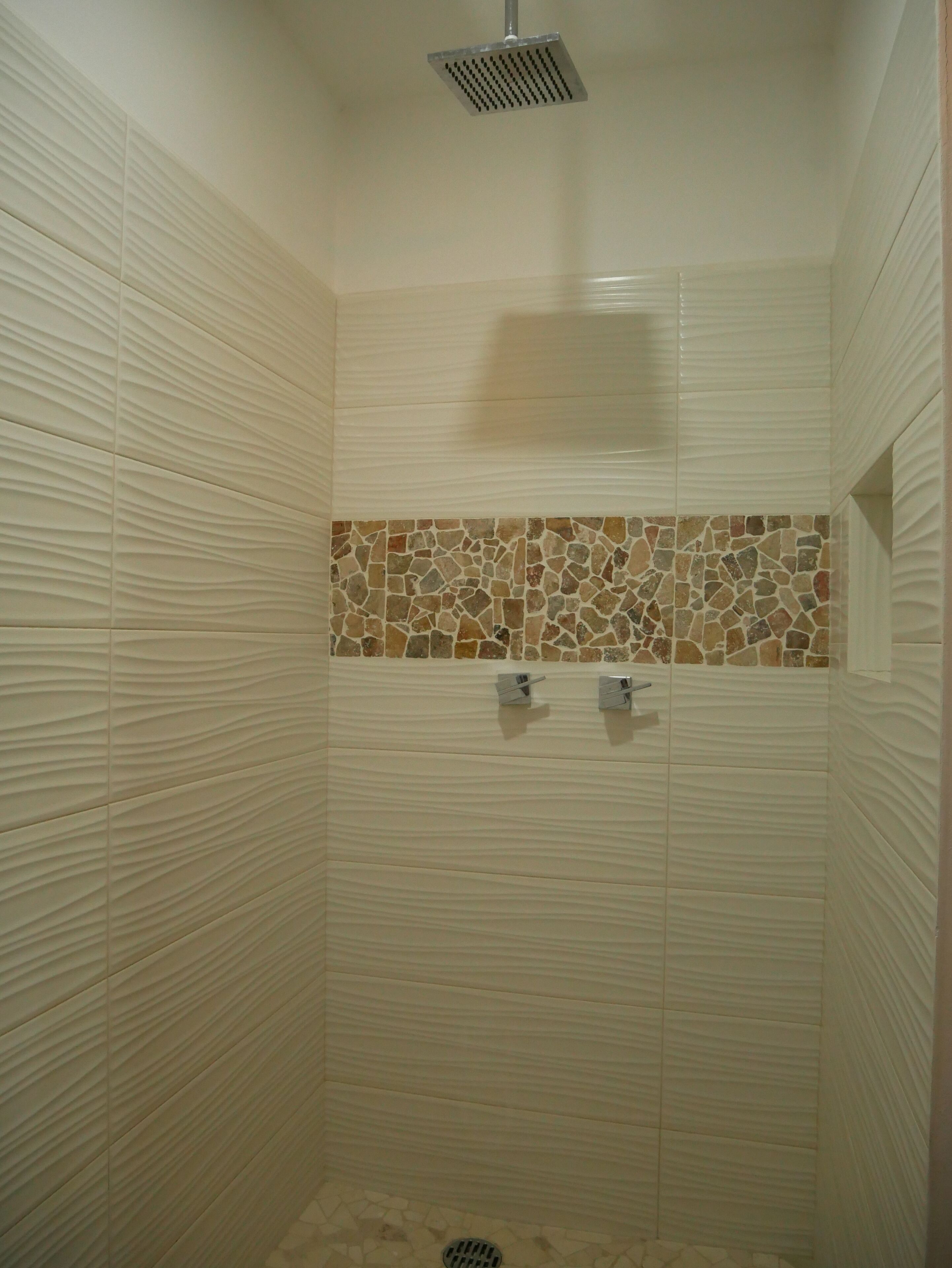 A shower with a textured wall and a mosaic tile border.