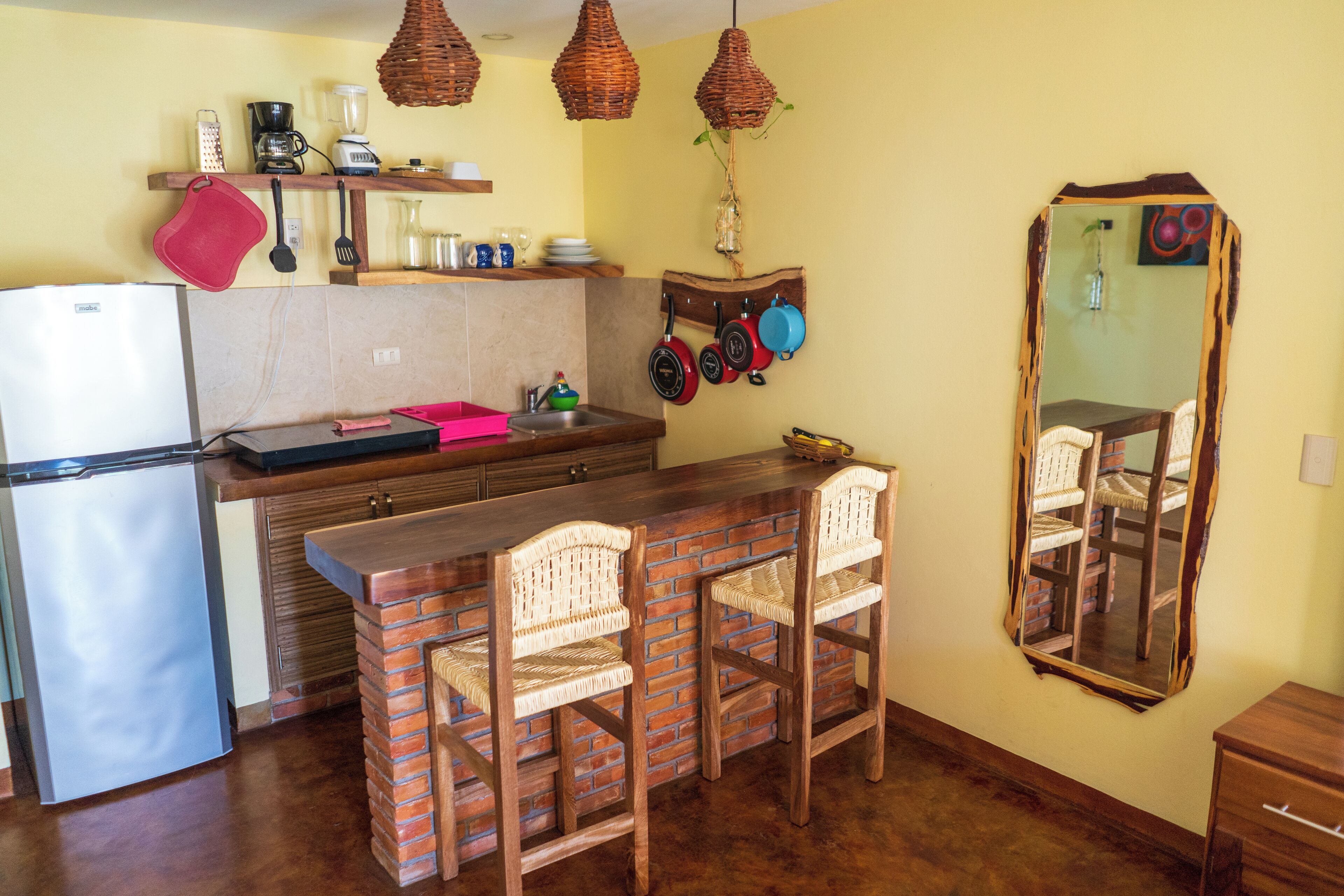A compact kitchen with a refrigerator, a wooden counter, and a bar area with two wicker chairs.