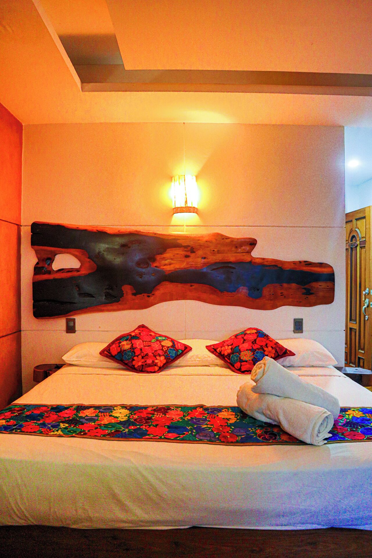 Une chambre d’hôtel avec une grande tête de lit en bois, une couvre-lit à motifs floraux et deux coussins décoratifs.