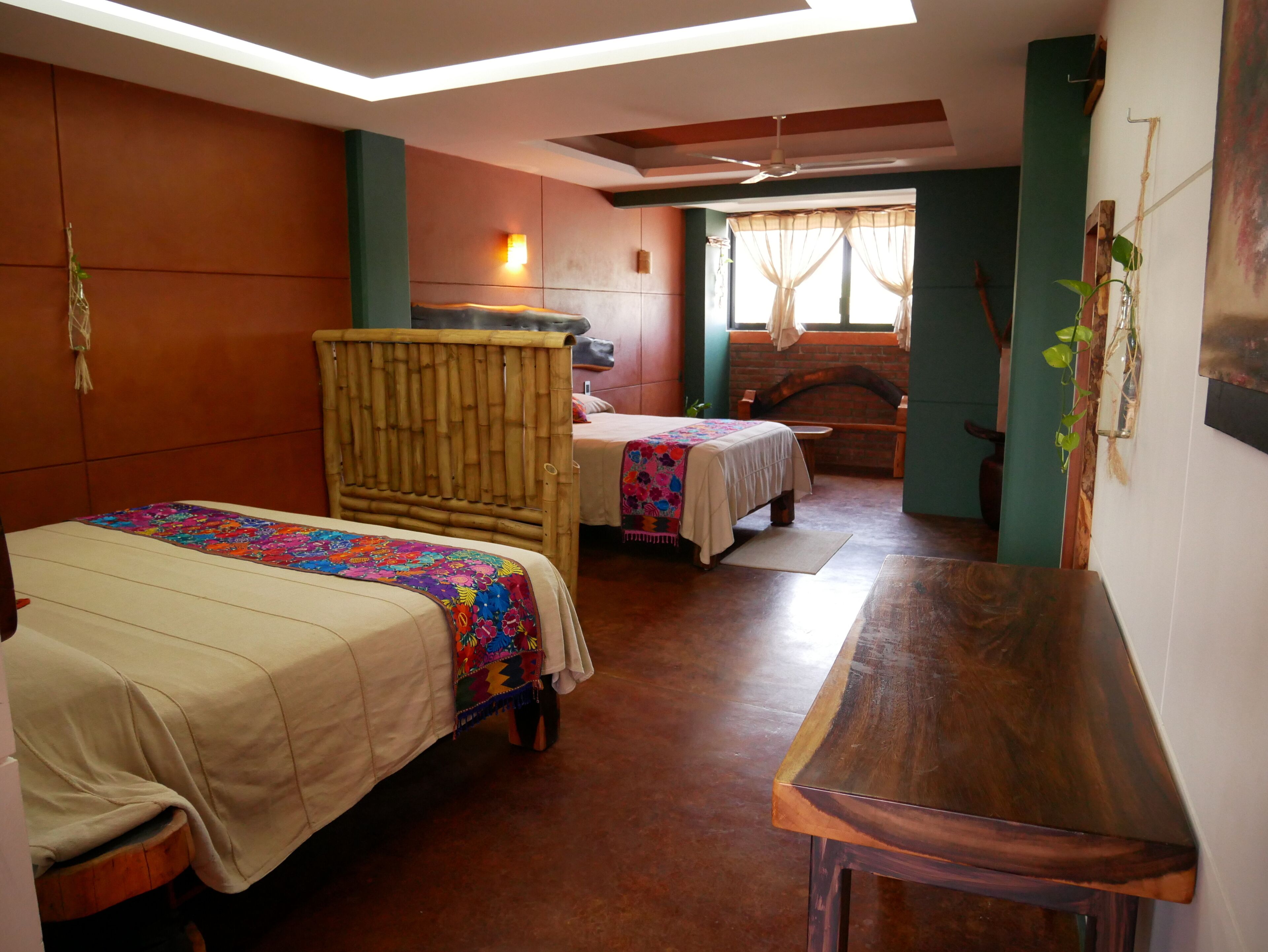 Ein Zimmer mit zwei Betten, einem Holztisch und einem Deckenventilator.