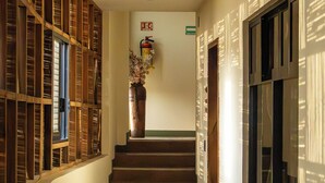A hallway with a staircase, wooden paneling on one side, a fire extinguisher, and a vase with flowers on the wall. - Madre Tierra Hotel & Coworking & Hostal (Puerto Escondido)