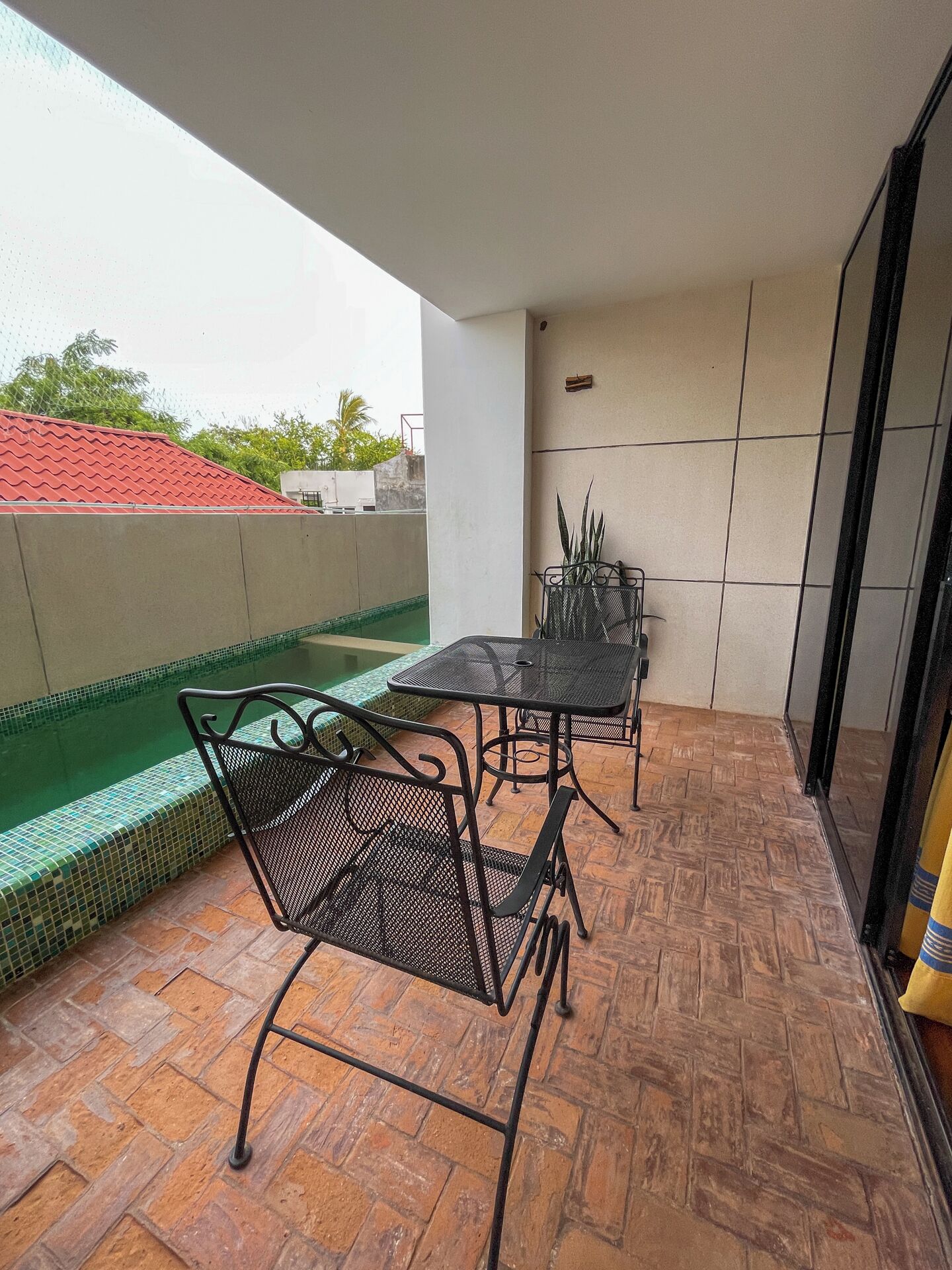Un balcón con suelo de baldosas, una mesa con sillas y una piscina pequeña.