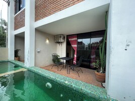 Una piscina con borde de azulejos, un área de patio con mesa y sillas, y una planta en maceta.