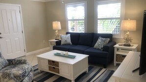 Ein Wohnzimmer mit einem dunkelblauen Sofa, zwei Beistelltischen mit Lampen, einem weißen Couchtisch, einem gemusterten Sessel und einem Streifenmuster-Teppich.