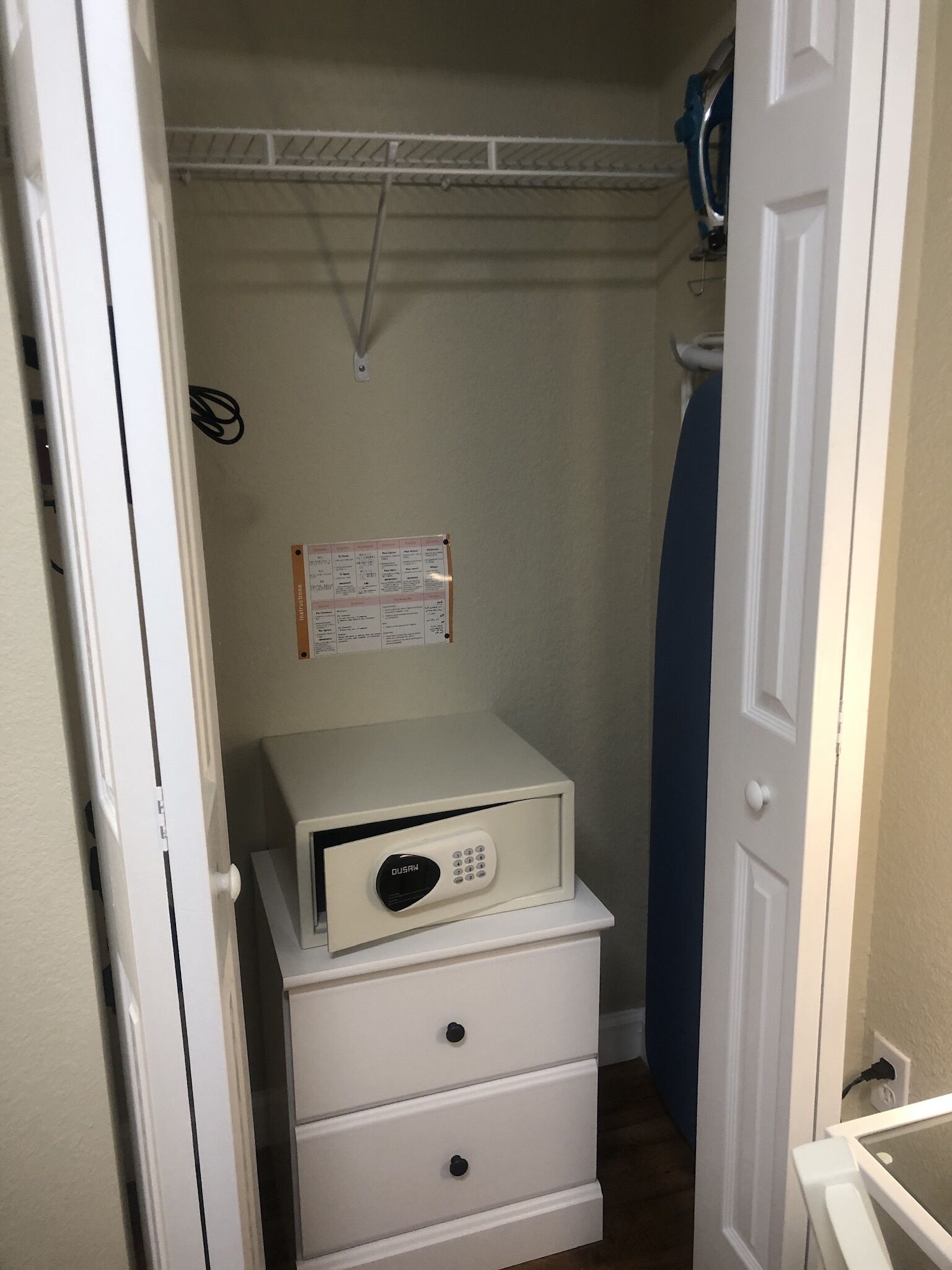A narrow hallway with a white door, a white dresser with drawers, and a small white shelf with a device on top.