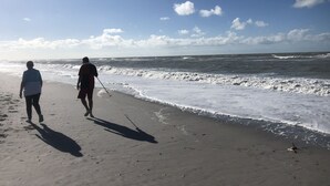 Zwei Personen laufen am sandigen Strand, während Wellen an die Küste brechen.