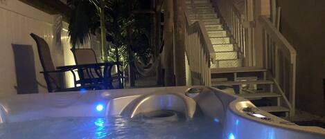A hot tub with blue lighting, a staircase, and a chair.