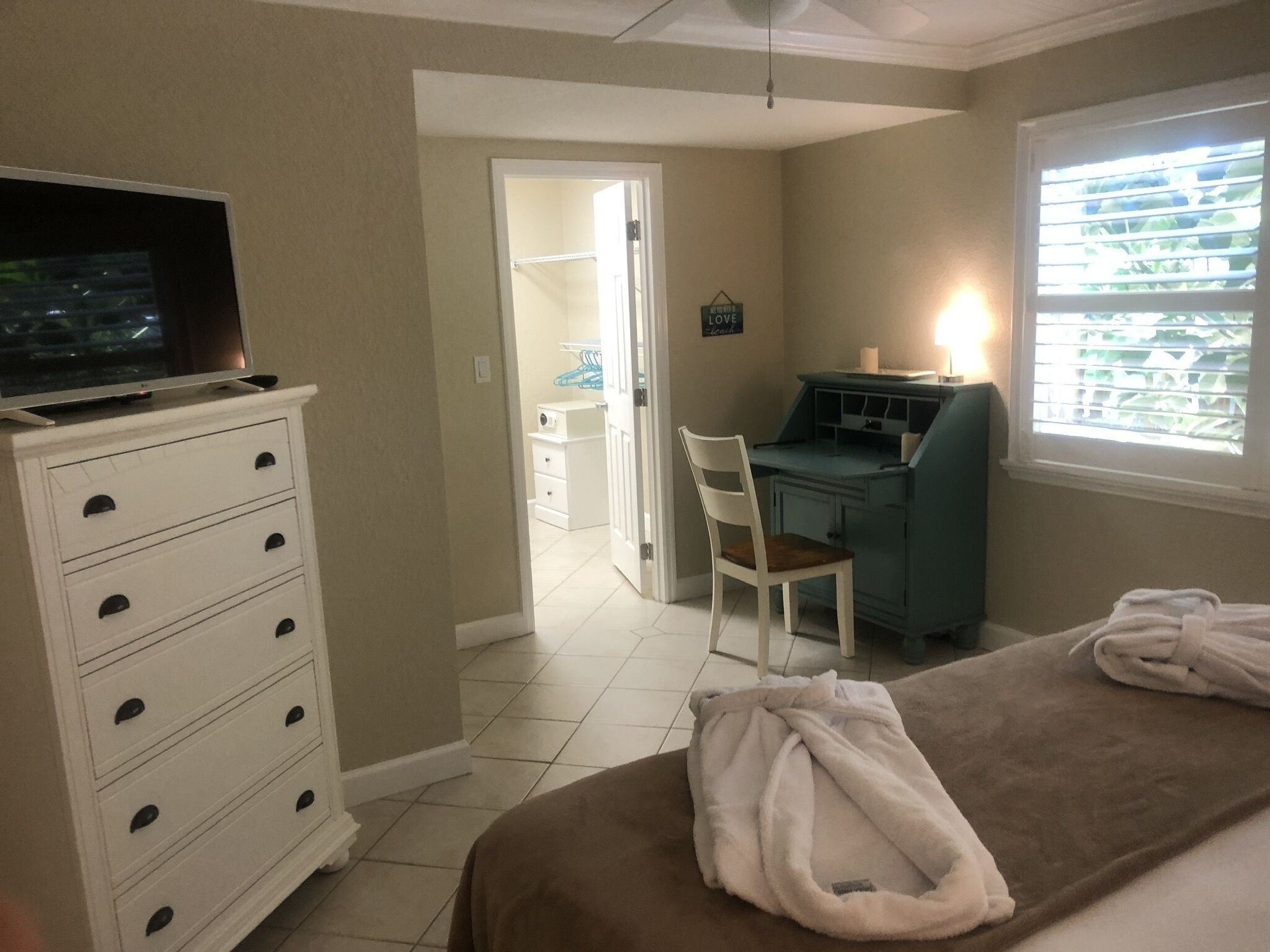 A bedroom with a bed, a desk, a chair, and a television on a dresser.