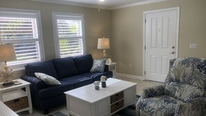 A living room with a dark blue sofa, a white coffee table, a patterned armchair, and a white door.