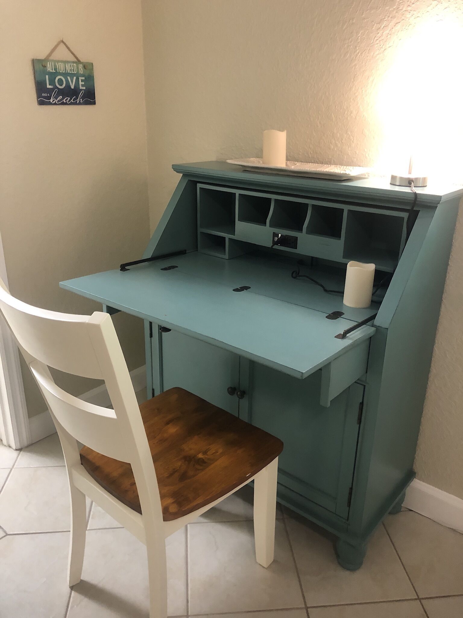 Een blauwgroene tafel met een witte stoel, een kaars en een bordje aan de muur.