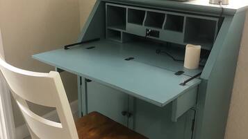 Een blauwgroene tafel met een witte stoel, een kaars en een bordje aan de muur.