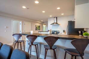 Una cocina moderna con una isla central, taburetes de bar y una campana extractora de acero inoxidable.