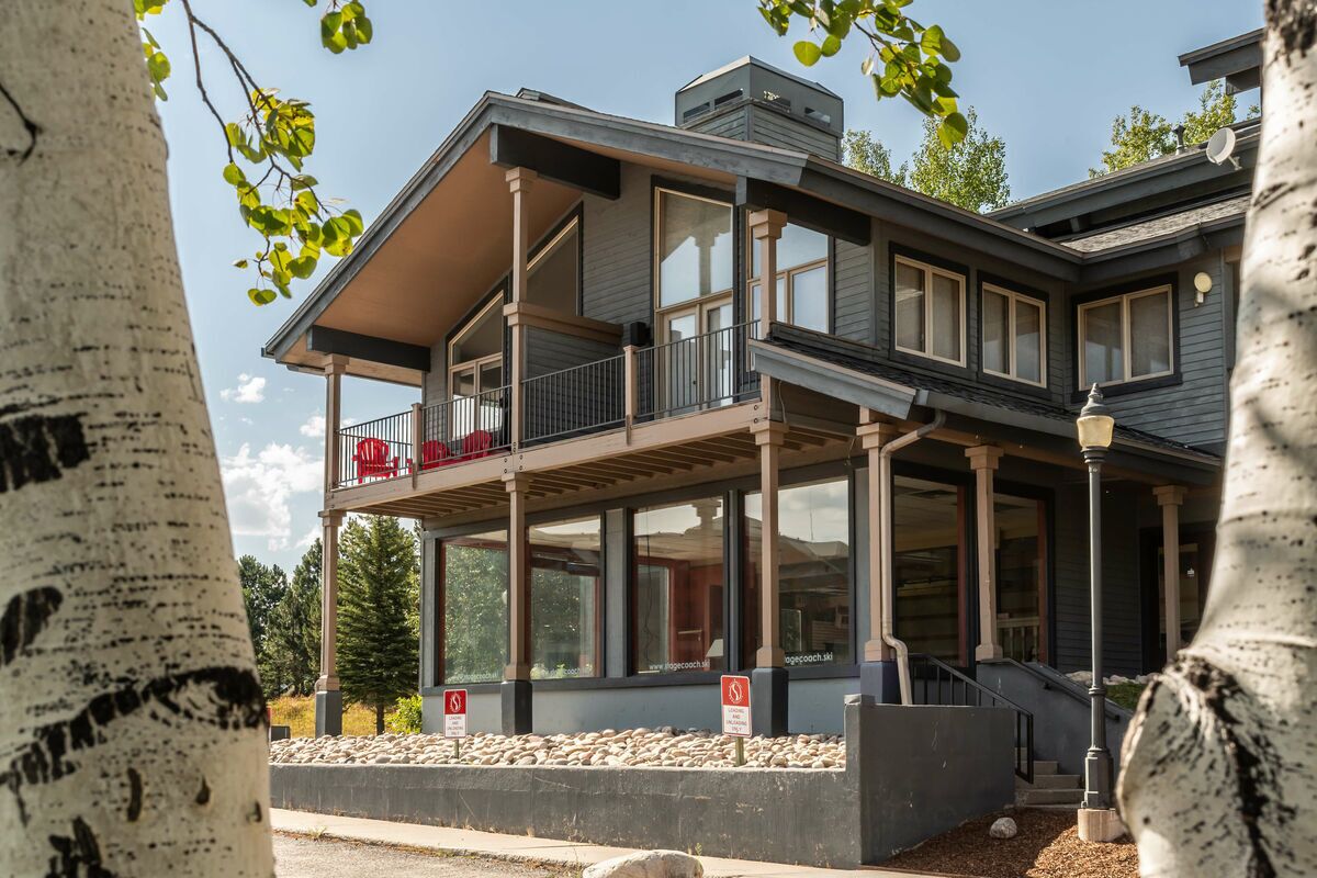 A two-story building with a balcony, large windows, and a stone foundation.