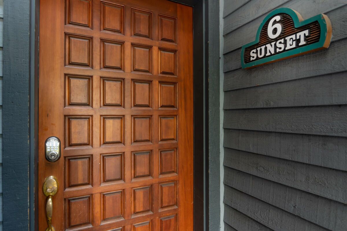 A wooden door with a keypad lock and a brass handle, and a house number sign indicating "6 Sunset".