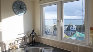 A kitchen with a large clock, a sink, and a window with a view of houses and water.