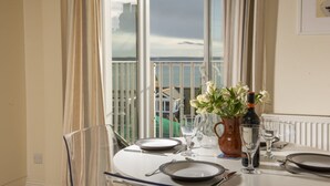 A dining table set for four with a view of the sea through large windows.