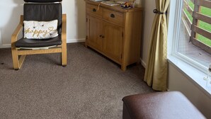 A room with a chair, a wooden cabinet, and a window with curtains. - Cheviot Luxury Lodge (Morpeth)
