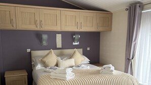 A bedroom with a bed, a nightstand, a wooden wardrobe, and a hanging light fixture. - Cheviot Luxury Lodge (Morpeth)