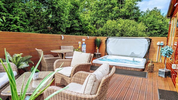 A wooden deck with wicker furniture, a hot tub, and a small plant. - Cheviot Luxury Lodge (Morpeth)