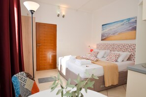A hotel room with a bed, a desk, a lamp, a door, and a painting of the sea. - Apartments Tea Kotor (Kotor)