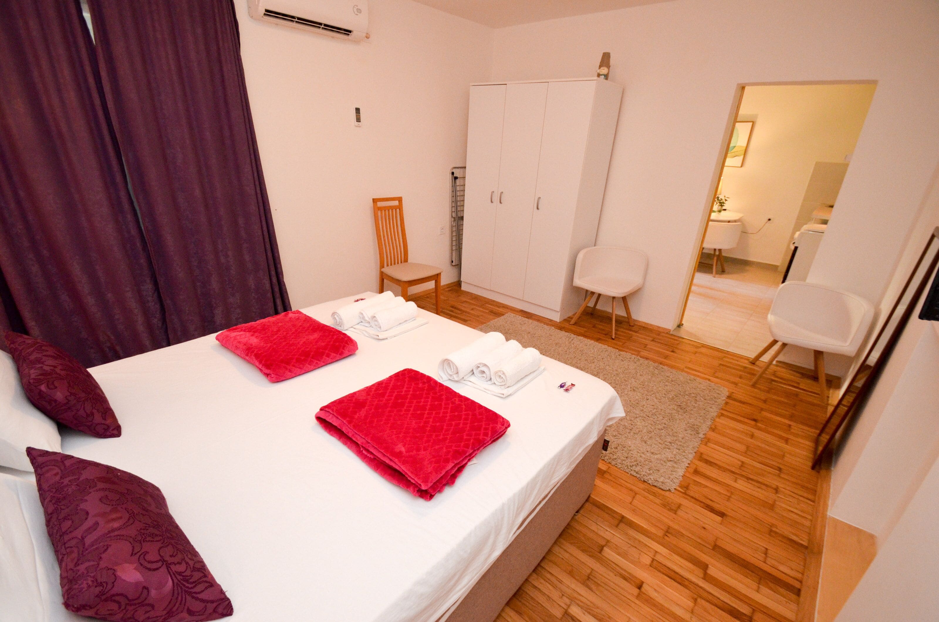Habitación de hotel con cama, dos sillas, un armario y un baño visible a través de una puerta abierta.