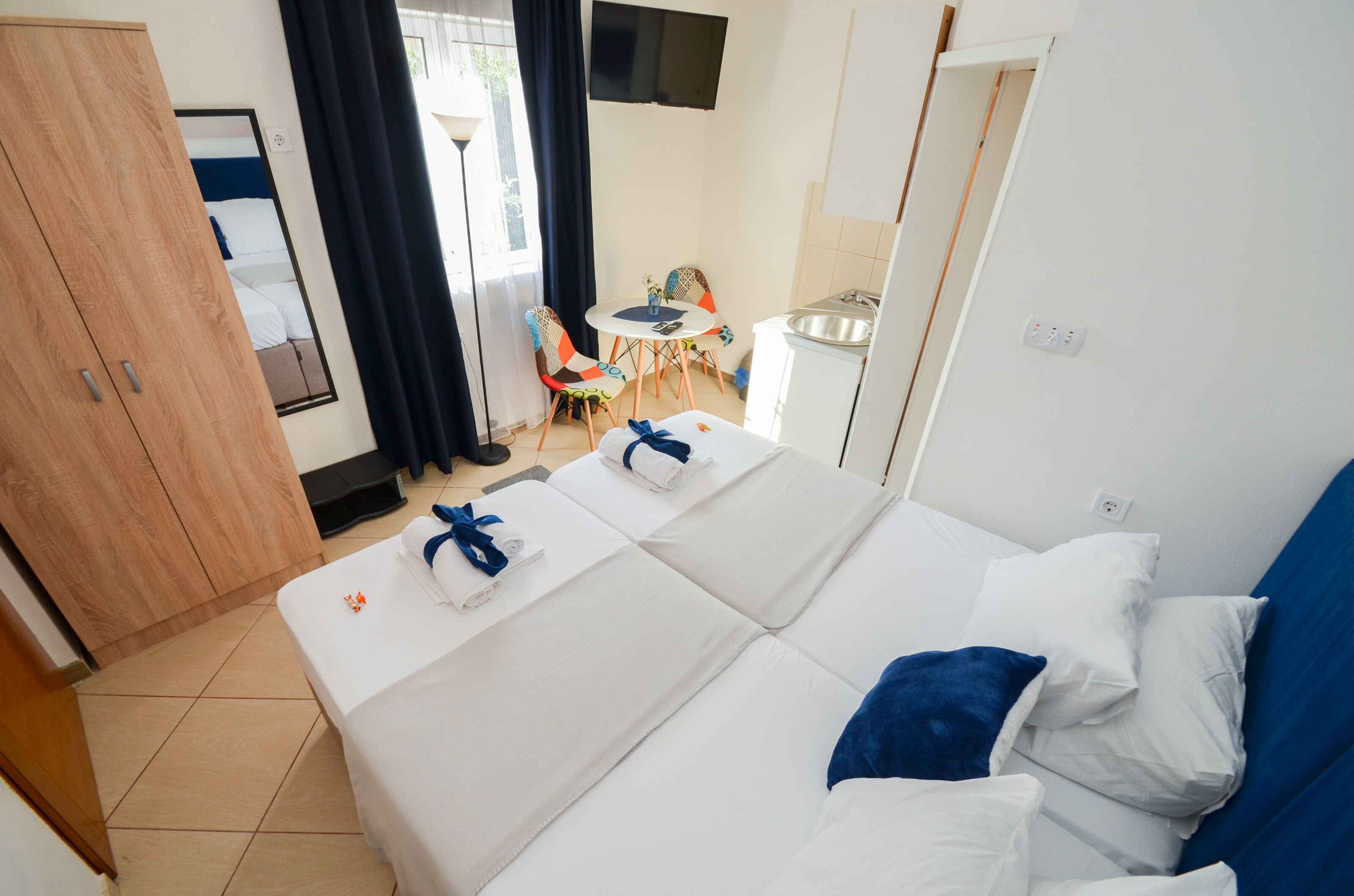 Ein Hotelzimmer mit Bett, kleinem Tisch, Stuhl, Fernseher und einer Küchenzeile.