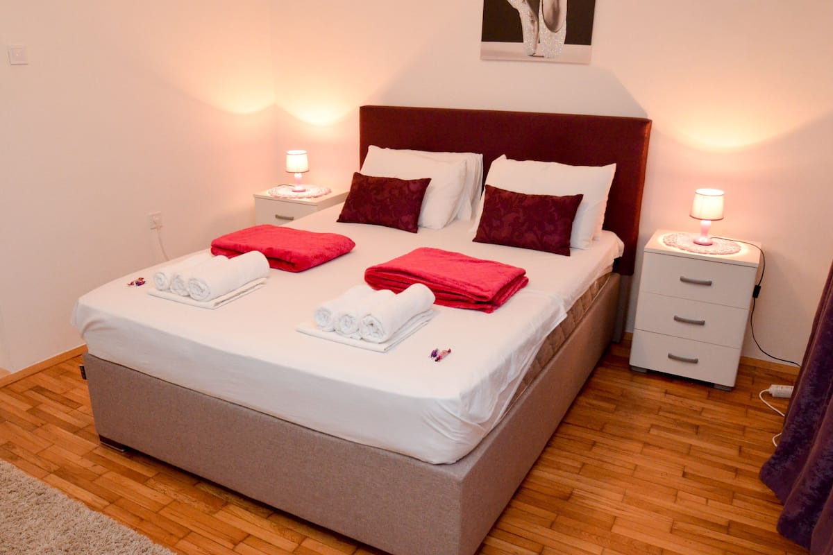 Ein ordentlich bezogenes Bett mit weißer und roter Bettwäsche, zwei Nachttische mit Lampen und ein Holzboden.