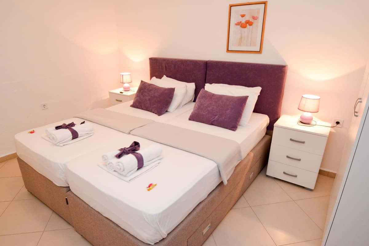 Ein Doppelbett mit violettem Kopfteil, zwei Nachttische mit Lampen sowie ein gerahmtes Bild an der Wand.