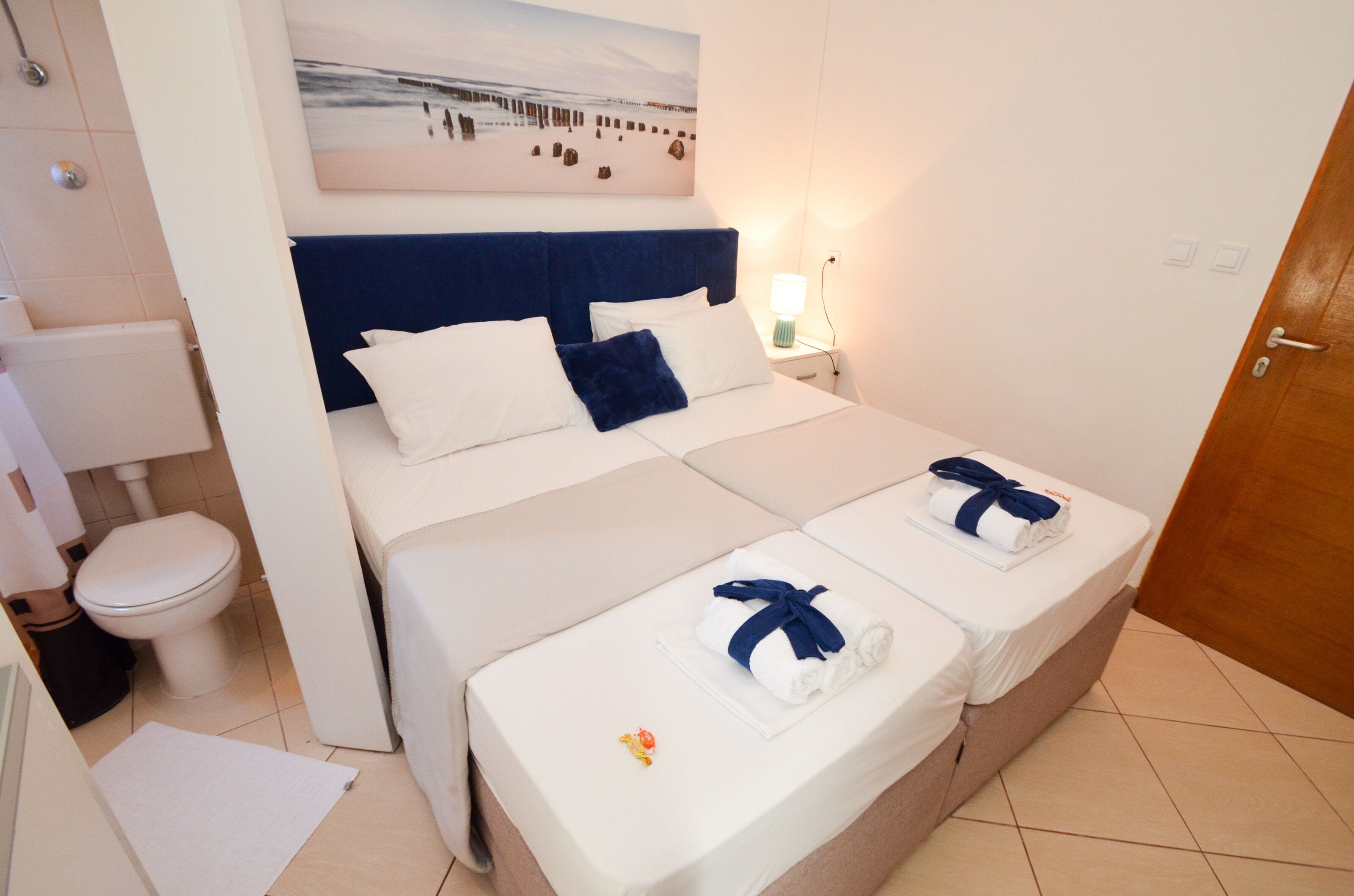 A hotel room with a large bed, a smaller bed, a bathroom, and a painting on the wall.