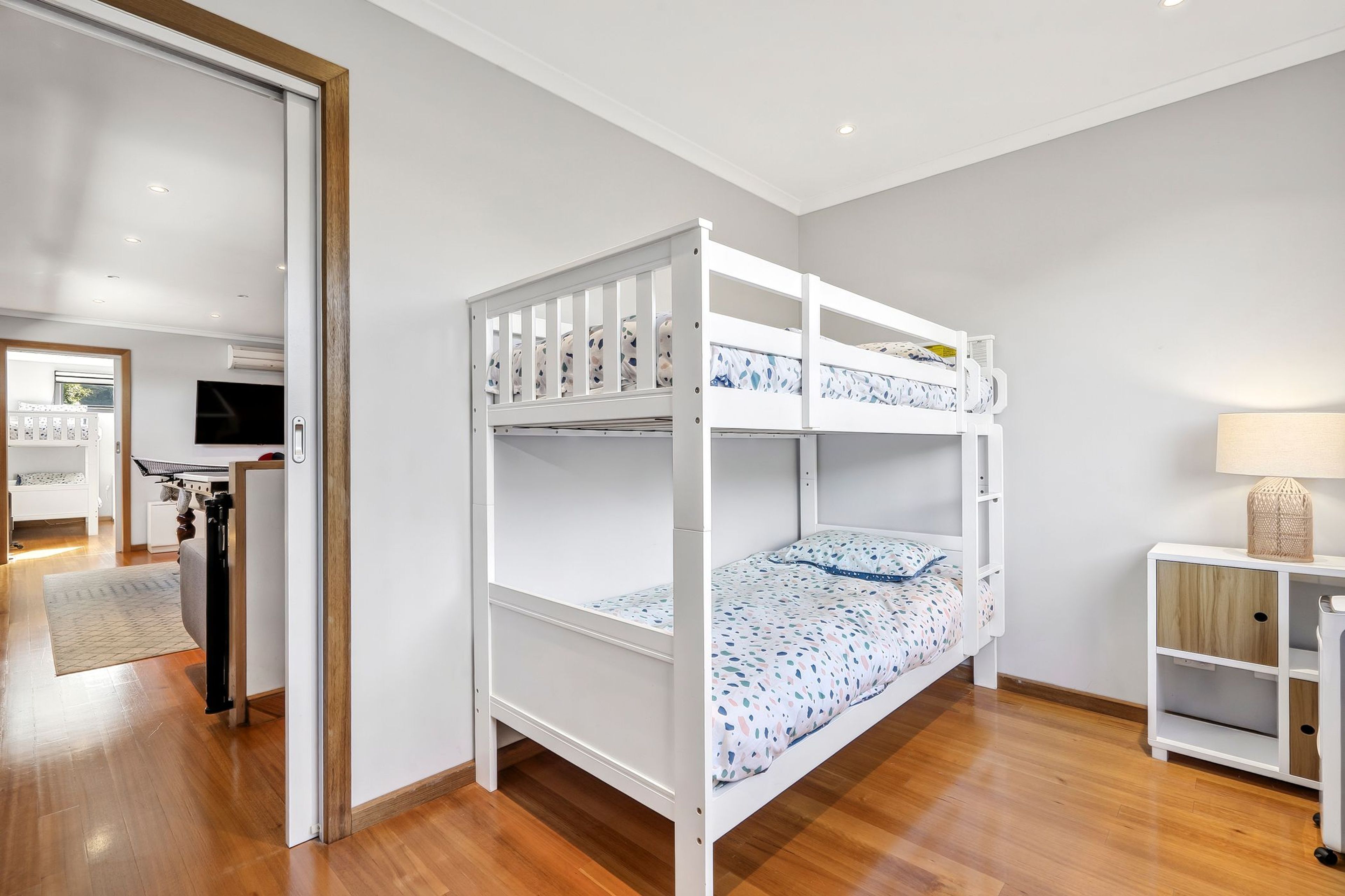 A bunk bed with a TV in the background, a desk with a lamp, and a wardrobe.