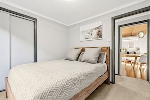 Une chambre à coucher avec un lit, une tête de lit en bois, un tableau au mur et une vue sur la pièce adjacente.