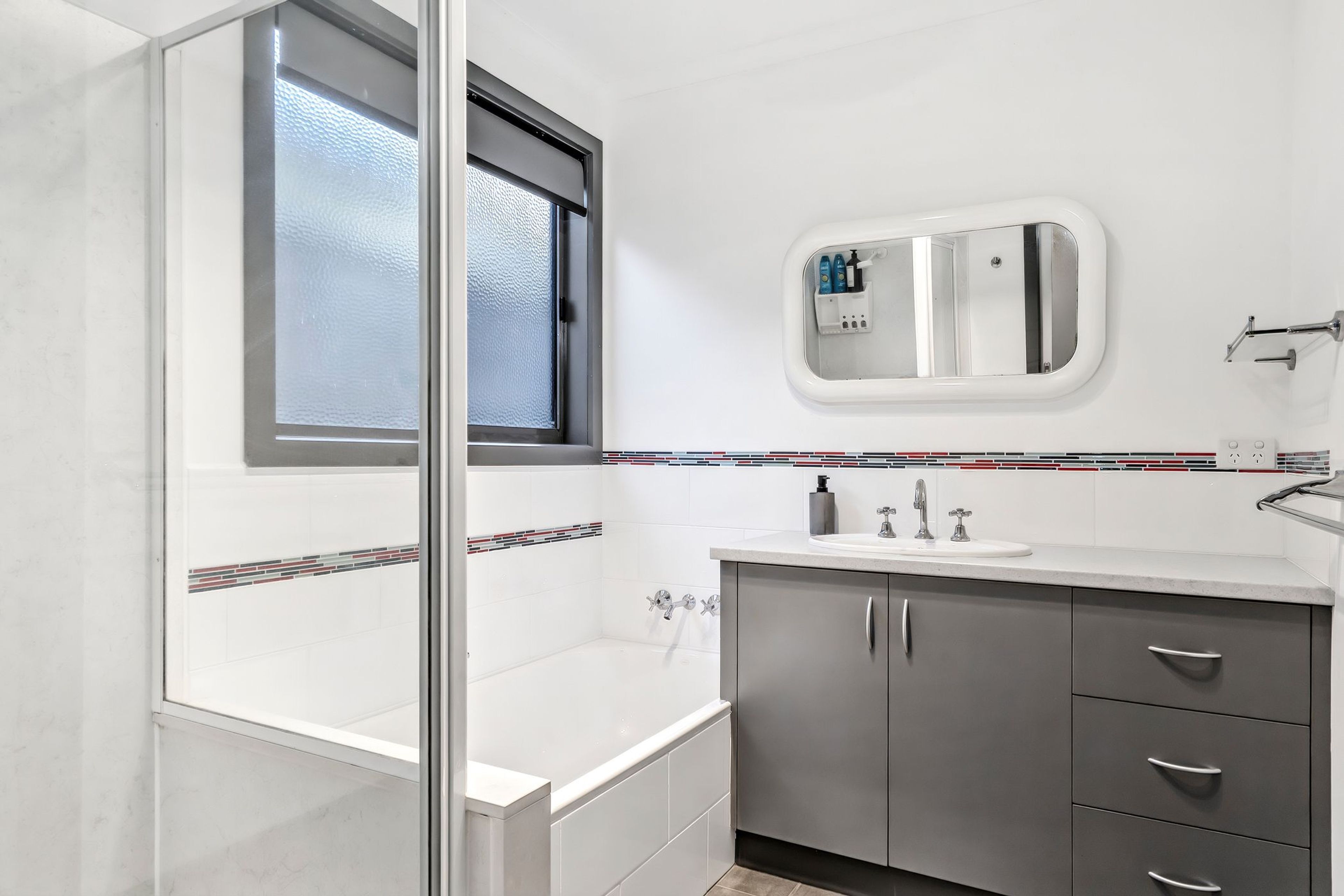 A modern bathroom with a glass shower enclosure, a vanity with a mirror, and a tiled backsplash.